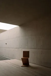 A minimalist, modern concrete room with a unique wooden chair.