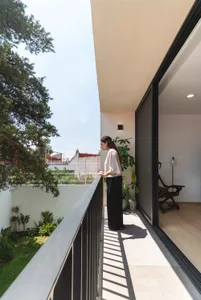A woman standing on a modern residential balcony with concrete and glass elements.