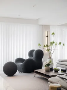 Minimalist living room with black armchair, white curtains, and potted plant.