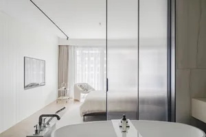 Modern minimalist bedroom featuring a glass door, wood floors, and neutral textiles.