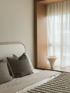 A minimalist bedroom with white bedding, cushions, and a lamp.
