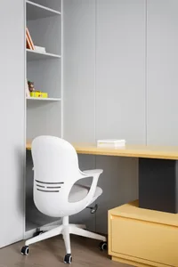A minimalist home office with a white ergonomic chair, desk with books, and storage unit.