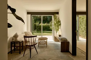 A minimalist living room featuring a stone floor, a white couch, a wooden chair, and a bamboo plant.
