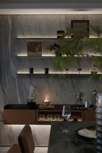 A sleek, modern bar counter featuring a combination of marble and glass materials, with shelves displaying decorative items.