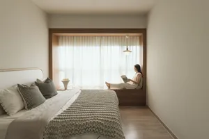 A modern bedroom with a bed covered in textured fabric, a window seat, and a person reading a book.