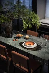 A modern dining room with a marble table and chairs, decorative greenery, and a candle.