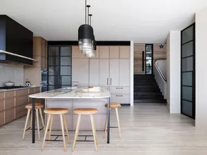 A modern kitchen featuring a marble island, wooden cabinets, and black metal accents.