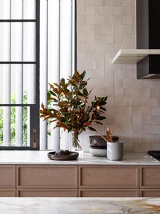 A modern kitchen with wooden cabinets and marble countertops featuring a potted plant and kitchen utensils.