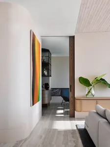 A modern interior design featuring a living room with a built-in bar area, curved walls, and a colorful abstract artwork.