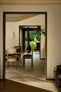 Modern minimalist dining room featuring a natural wood dining table and chairs, with a view of the outdoors through large win