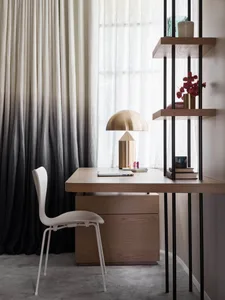 A modern workspace featuring a wooden desk with a brass lamp, and tall black and white curtains