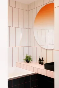 Modern bathroom with large black and white ceramic tiles, black countertop, and orange-hued wall above