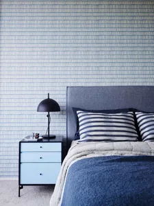 A modern bedroom with blue and white striped bedding, a fabric headboard, and a light blue bedside table with a black lamp an