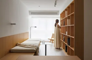 A minimalist bedroom with a wooden panel bed, floor lamp, and wooden bookshelf.