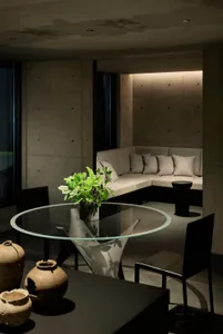 A minimalist living room featuring a concrete wall, circular glass table, and black chairs.