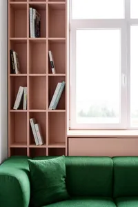 A modern living room featuring a green sofa with a bookshelf and a window.