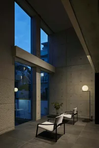 A modern interior living room featuring minimalist design with concrete walls and floor, large windows, and two armchairs.