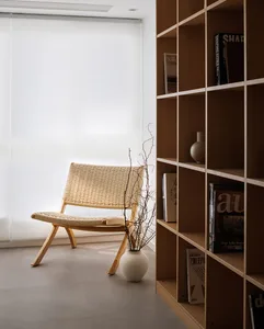 Modern living room with a wood and rattan chair, white vase with branches, and a bookshelf.