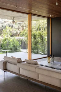 A modern living room featuring a wooden ceiling and large windows overlooking greenery.