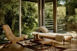A minimalist living room with wooden furniture, fabric cushions, and glass walls.