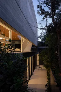 Modern concrete exterior of a house with large windows and garden at dusk.
