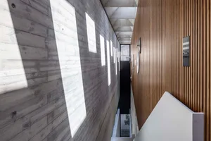 Modern corridor with concrete and wood walls, light filtering through windows.