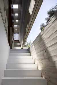 A modern interior staircase with white steps and a concrete wall, illuminated by natural light from the window.
