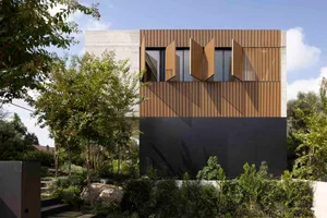 A modern house with wooden panels and concrete structure, featuring large windows with open shutters and surrounded by greene