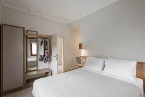 Minimalist bedroom with a white bed, wooden headboard, and simple decor.