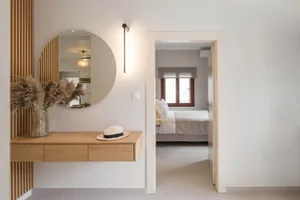 A minimalist bedroom featuring a wooden desk and white walls, with a view into the adjoining room.