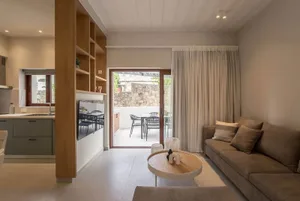 A modern, minimalist living room with concrete walls, wooden furniture, and a flat-screen TV mounted on the wall.