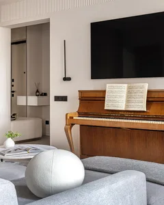 A modern, minimalist living room with a wooden piano, gray furniture, and a plant.