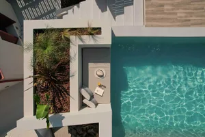 Sunlit poolside concrete lounging area with green plants, cushions, and a book on a bench
