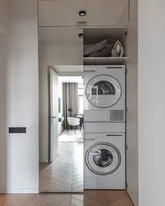 Modern minimalist laundry room featuring sleek metal appliances and glass panels, with a wooden herringbone floor.