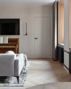 A modern living room featuring light-colored wood flooring, a grey sofa on a dark rug, and a piano with sheet music.