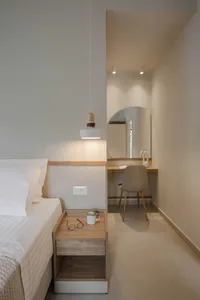 A minimalist bedroom with a bed, nightstand, pendant light, and a desk area with a chair and a desk lamp.