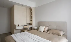 Modern, minimalist bedroom with a beige headboard bed, wooden floor, and built-in desk with shelves.