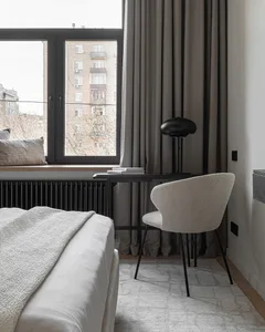 Minimalist bedroom featuring a white bed with textured fabric, a black desk, and a beige chair.