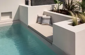 Modern, minimalist outdoor seating area with concrete walls and cushions by a pool.