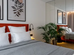 A minimalist bedroom with a textured fabric headboard, potted palm plant, and modern abstract artwork.