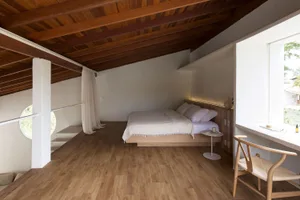Modern minimalist bedroom with wooden floor and furniture, high ceiling with exposed beams.