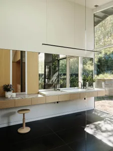 A modern bathroom featuring a floating vanity with dark wood cabinets, glass shower enclosure, and large windows overlooking 