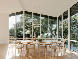 A modern dining room featuring a large table surrounded by wooden chairs, with a hanging circular light fixture and large win