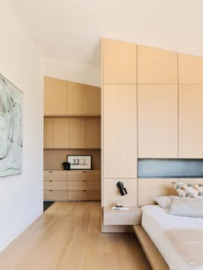A minimalist bedroom with wood finishes, including a bed, nightstand, and built-in storage cabinets.