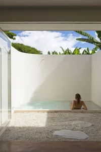 Person relaxing in a modern residential concrete pool with lush greenery and blue sky in the background.
