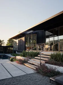Modern residential exterior featuring wood, glass, and concrete materials with a terrace.