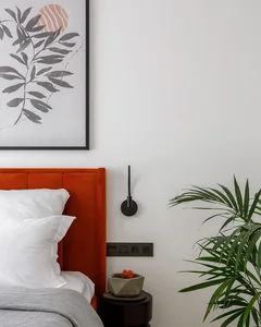 A modern bedroom featuring an orange velvet headboard, white pillows, and a grey throw blanket, complemented by a concrete be