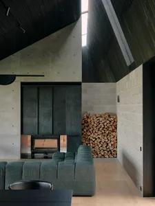 A spacious industrial-style living room featuring a concrete fireplace and numerous stacked logs.