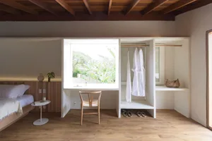 A minimalist bedroom with a large window, a wooden chair, and a view of an indoor garden.