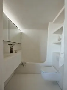 A minimalist bathroom with concrete materials, featuring a sink, mirror, shelf, bathtub, and toilet.